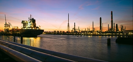 A sea freight vehicle in a panoramic cityscape at dusk with the ExxonMobil Rotterdam refinery in the background.