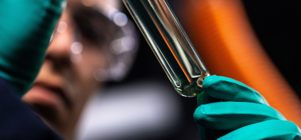 A lab technician wearing safety gloves holding the results of an experiment in a vial.