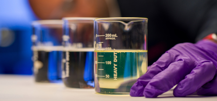 A lab technician wearing protective safety equipment looking at three beakers filled with Group II/II+ Base Stocks.