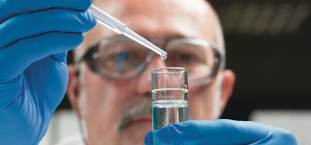 Lab technician wearing safety equipment while precisely measuring liquid with a syringe and vial.