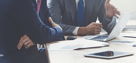 Two men sit in front of a laptop in a business meeting