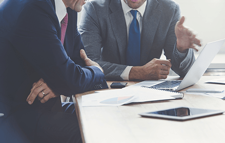 Two men sit in front of a laptop in a business meeting