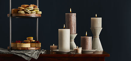 pillar candles on table with food trays next to them and  dark background