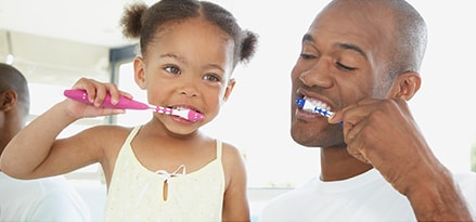 Father and daughter brushing their teeth together