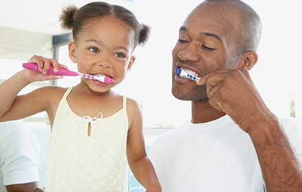 Father and daughter brushing their teeth together